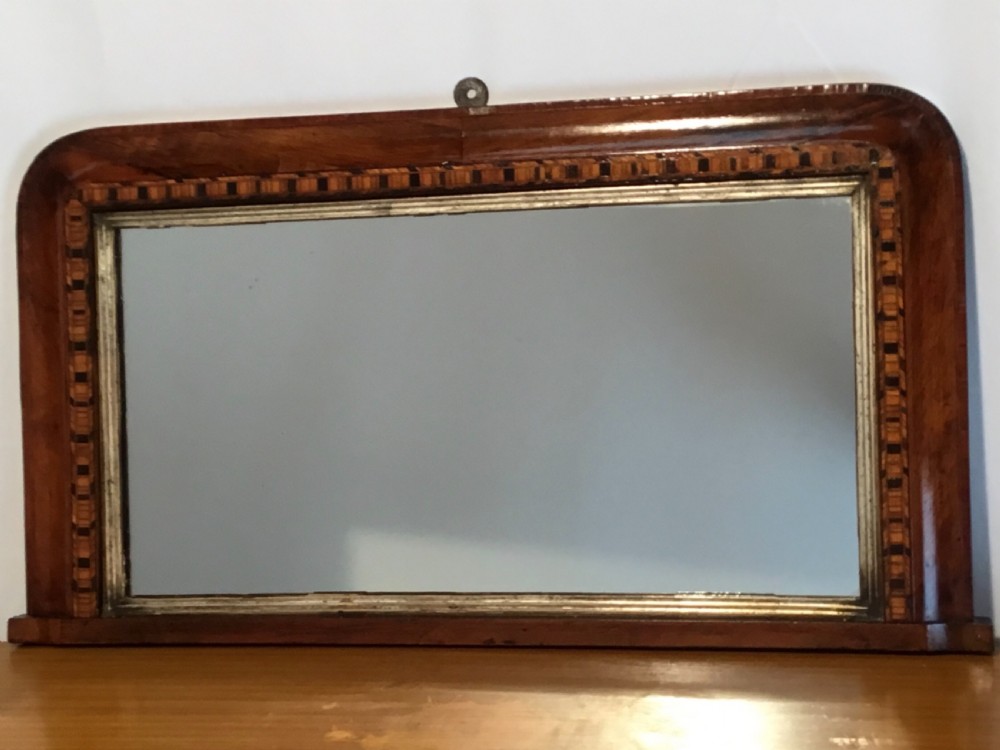 A Victorian walnut overmantel mirror featuring a low rectangular frame with rounded top corners, detailed geometric wood inlay, and a gilded inner slip surrounding a reflective mirror plate. View IV