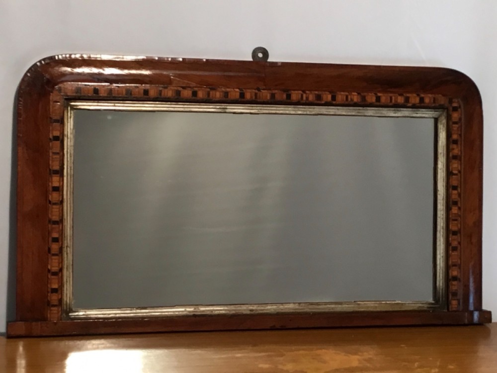 A Victorian walnut overmantel mirror featuring a low rectangular frame with rounded top corners, detailed geometric wood inlay, and a gilded inner slip surrounding a reflective mirror plate. View V