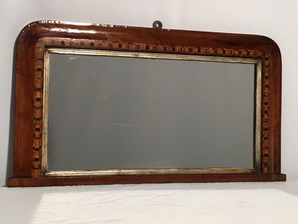 A Victorian walnut overmantel mirror featuring a low rectangular frame with rounded top corners, detailed geometric wood inlay, and a gilded inner slip surrounding a reflective mirror plate. View VIII