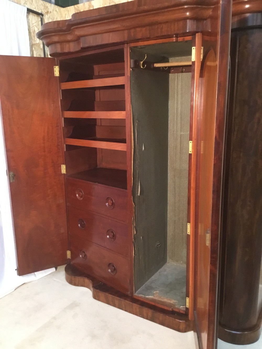 A Mid Victorian flame mahogany compactum wardrobe featuring a central arched mirror door flanked by curved side sections beneath a deep moulded cornice. View XIV