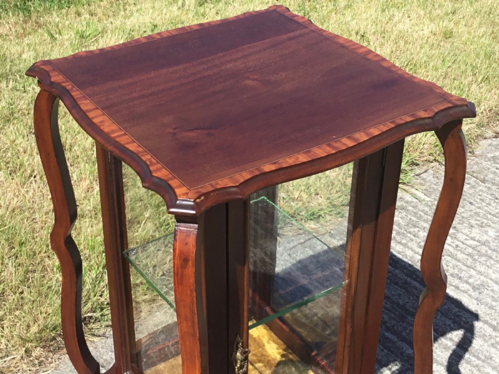 An antique mahogany bijouterie cabinet featuring four slender curved outer legs, glass side panels, a central glass shelf, and a glazed front door. View V