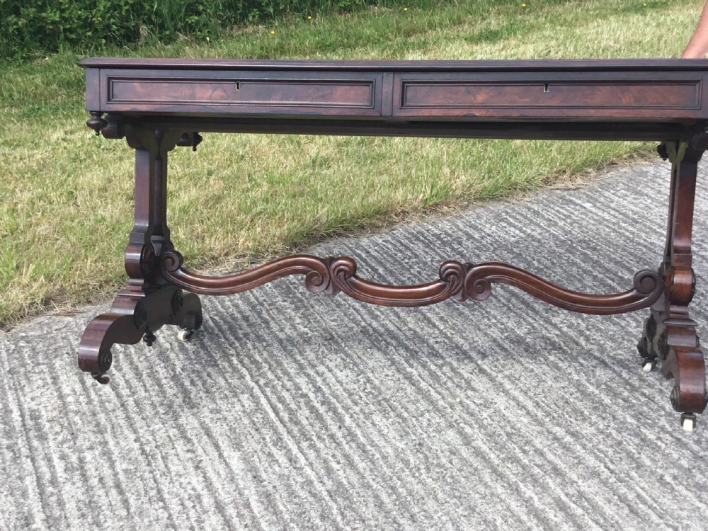 A William IV rosewood library table featuring a rectangular top, frieze drawers, turned trestle end supports, a carved stretcher, and scroll feet on castors. View II