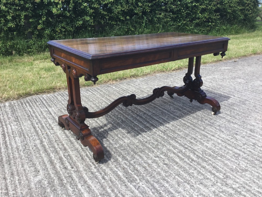 A William IV rosewood library table featuring a rectangular top, frieze drawers, turned trestle end supports, a carved stretcher, and scroll feet on castors. View VIII