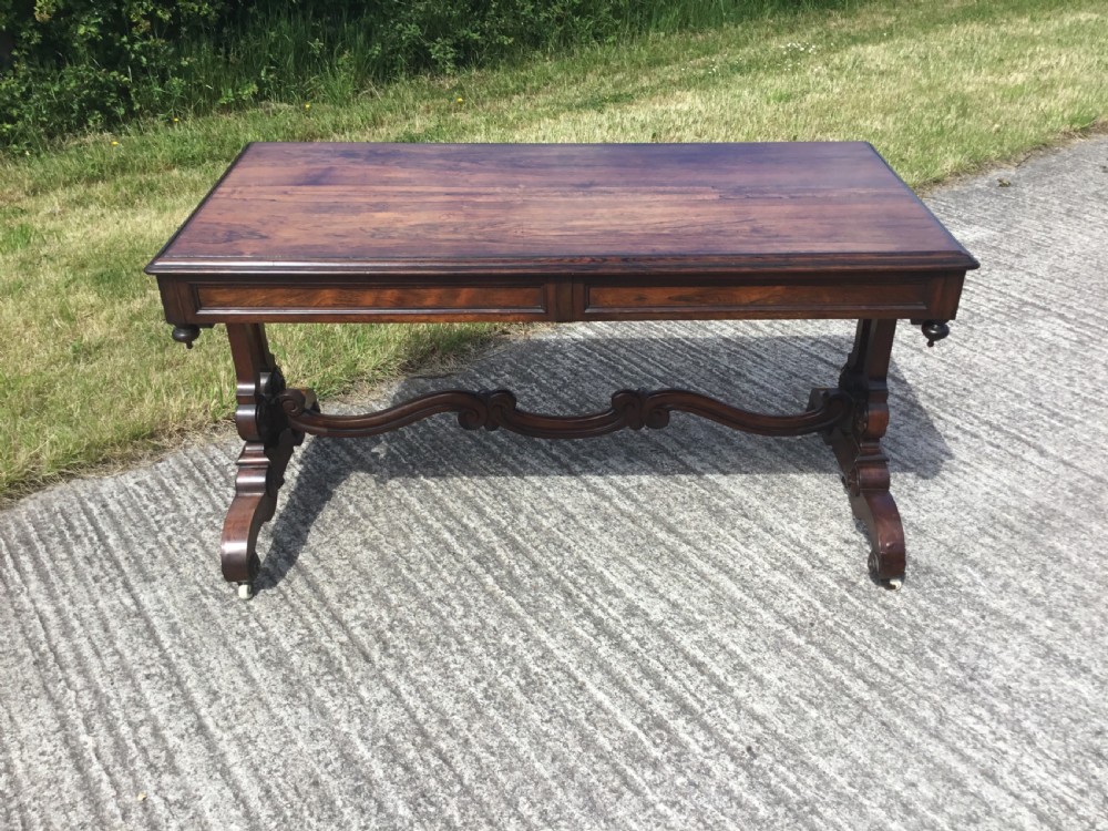 A William IV rosewood library table featuring a rectangular top, frieze drawers, turned trestle end supports, a carved stretcher, and scroll feet on castors. View IX