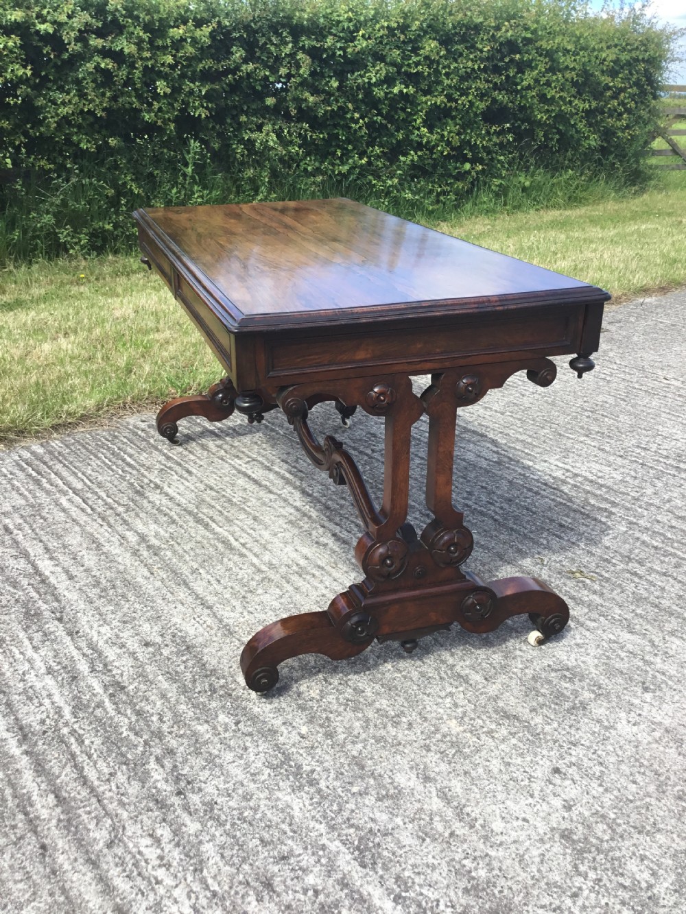 A William IV rosewood library table featuring a rectangular top, frieze drawers, turned trestle end supports, a carved stretcher, and scroll feet on castors. View XI