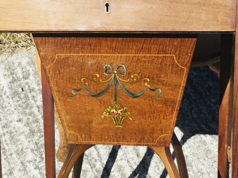 An antique square wooden work table featuring a painted portrait medallion surrounded by floral garlands on the lid, supported by square tapered legs with arched stretchers. View V