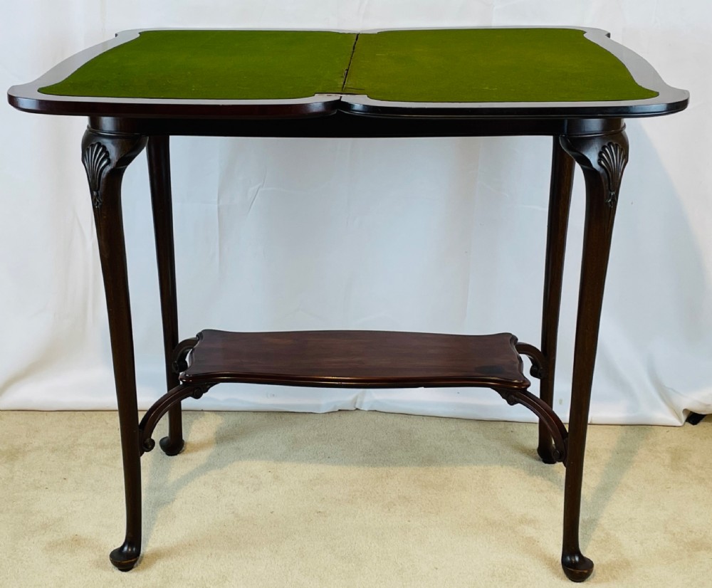 A dark mahogany Queen Anne style fold-over card table featuring cabriole legs with shell-carved knees and a lower stretcher shelf. View XI