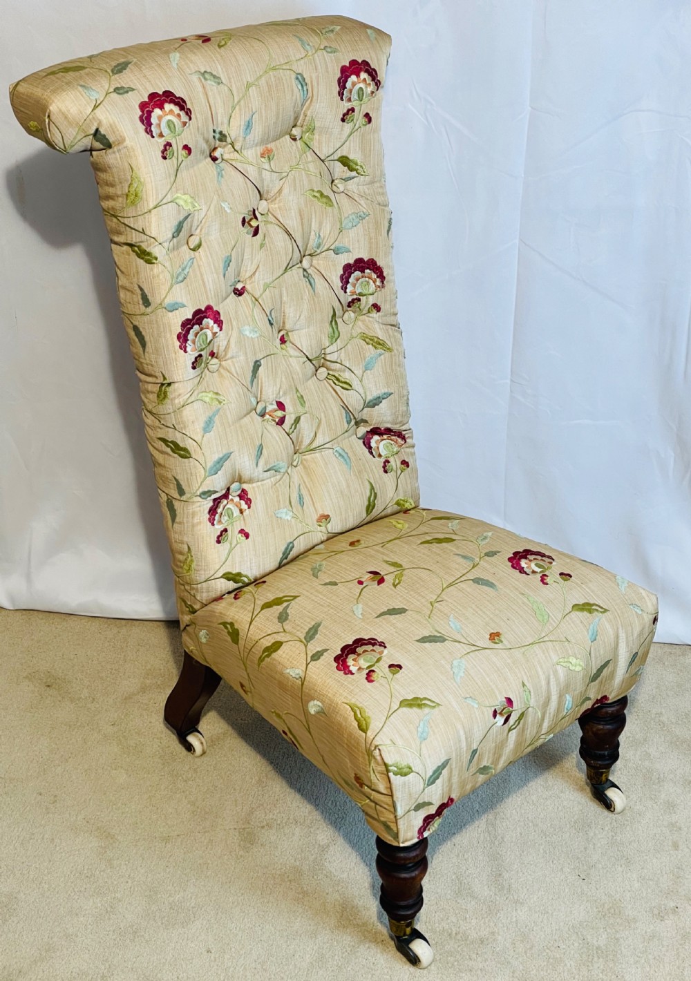 A Victorian Prie-Dieu chair featuring button-tufted cream upholstery with floral embroidery, supported on turned dark wood legs with ceramic castors.