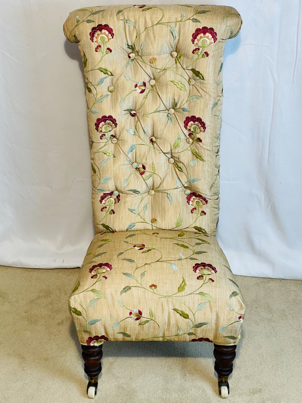 A Victorian Prie-Dieu chair featuring button-tufted cream upholstery with floral embroidery, supported on turned dark wood legs with ceramic castors. View IV