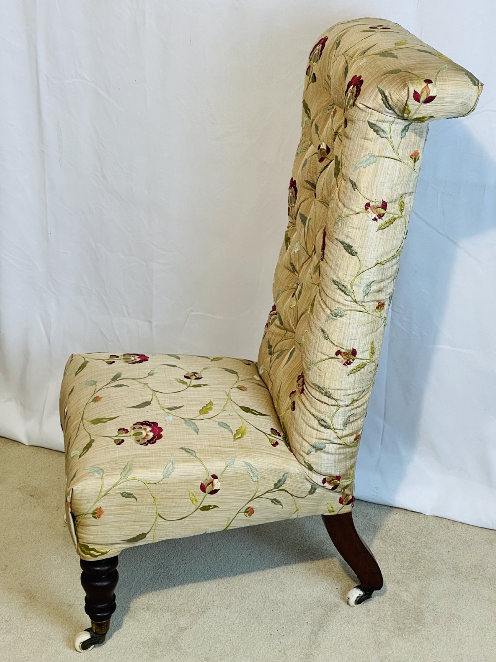 A Victorian Prie-Dieu chair featuring button-tufted cream upholstery with floral embroidery, supported on turned dark wood legs with ceramic castors. View V