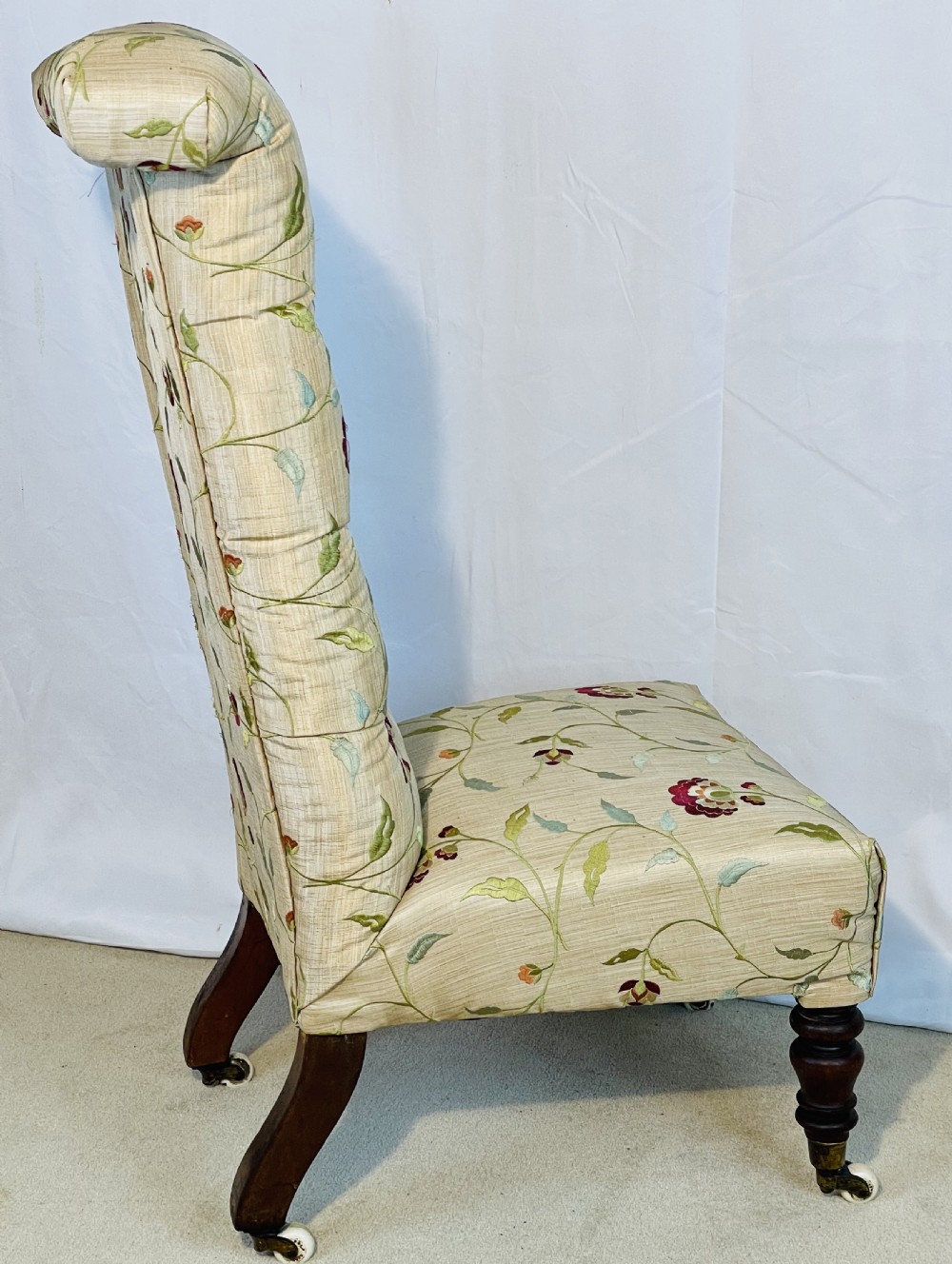 A Victorian Prie-Dieu chair featuring button-tufted cream upholstery with floral embroidery, supported on turned dark wood legs with ceramic castors. View X