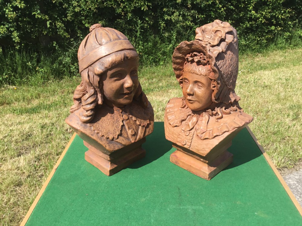 A pair of 19th-century terracotta portrait busts depicting a young boy wearing a cap and a young girl wearing a frilled bonnet.