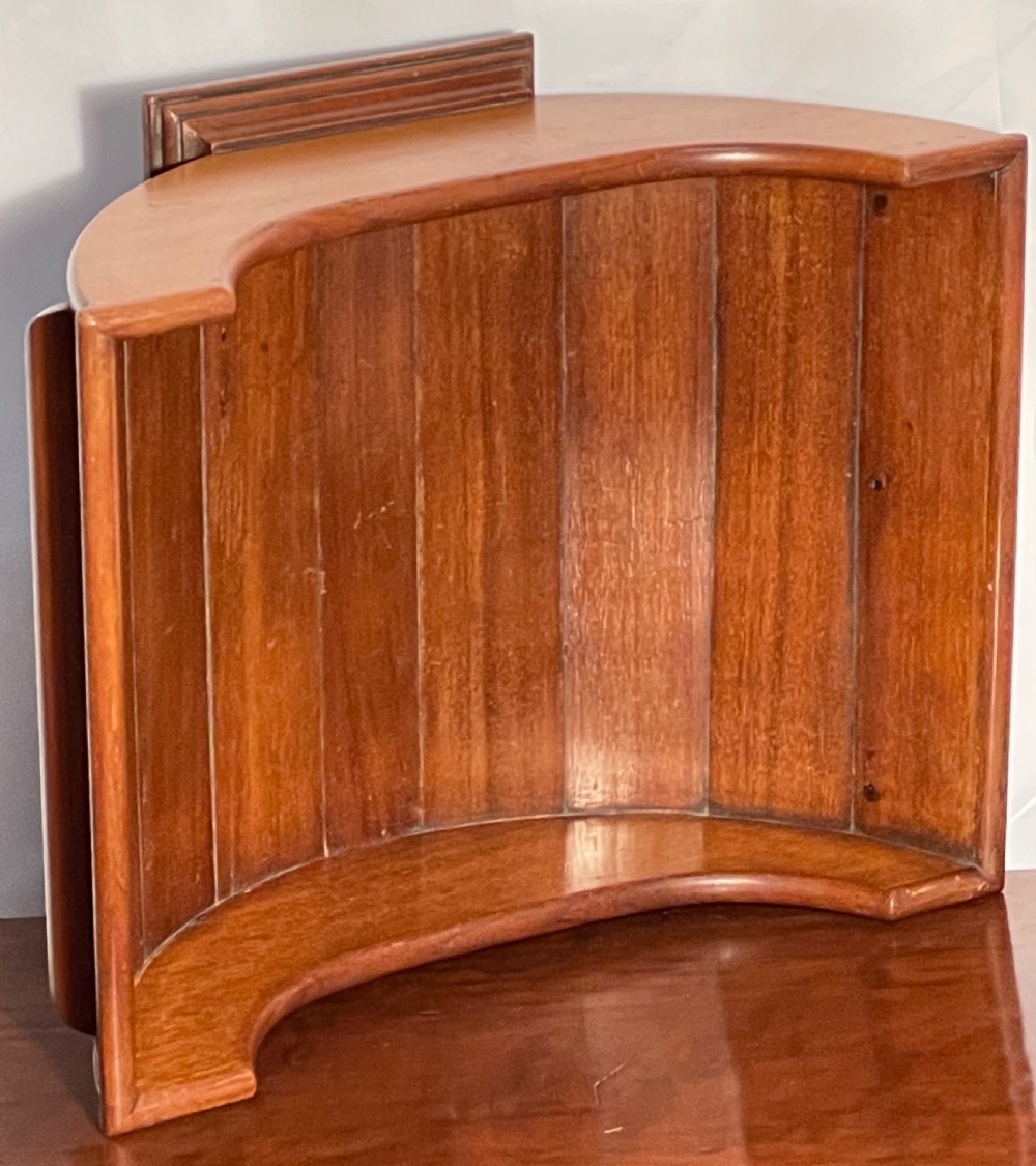 A mahogany wooden cheese cradle featuring a curved slatted trough mounted on a moulded rectangular plinth base. View III