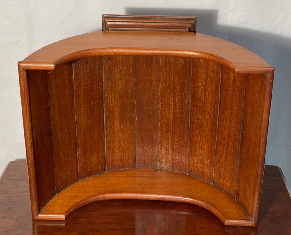 A mahogany wooden cheese cradle featuring a curved slatted trough mounted on a moulded rectangular plinth base. View V