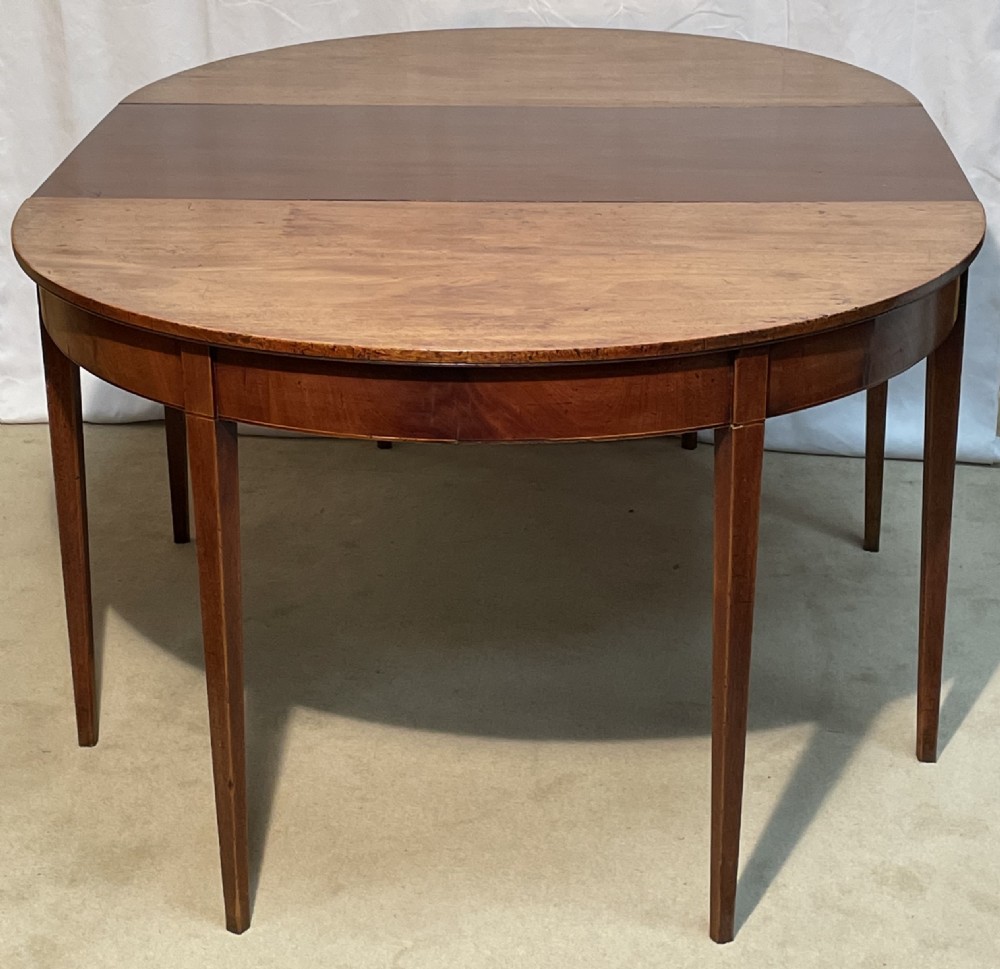 A Georgian mahogany extension dining table featuring a round top assembled from two demi-lune end sections and a central leaf, supported by slender square tapered legs.