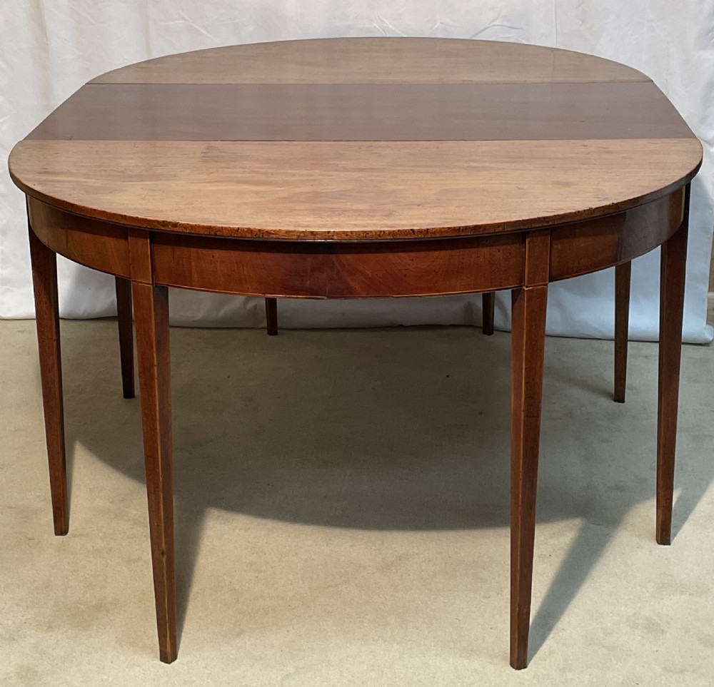A Georgian mahogany extension dining table featuring a round top assembled from two demi-lune end sections and a central leaf, supported by slender square tapered legs. View II