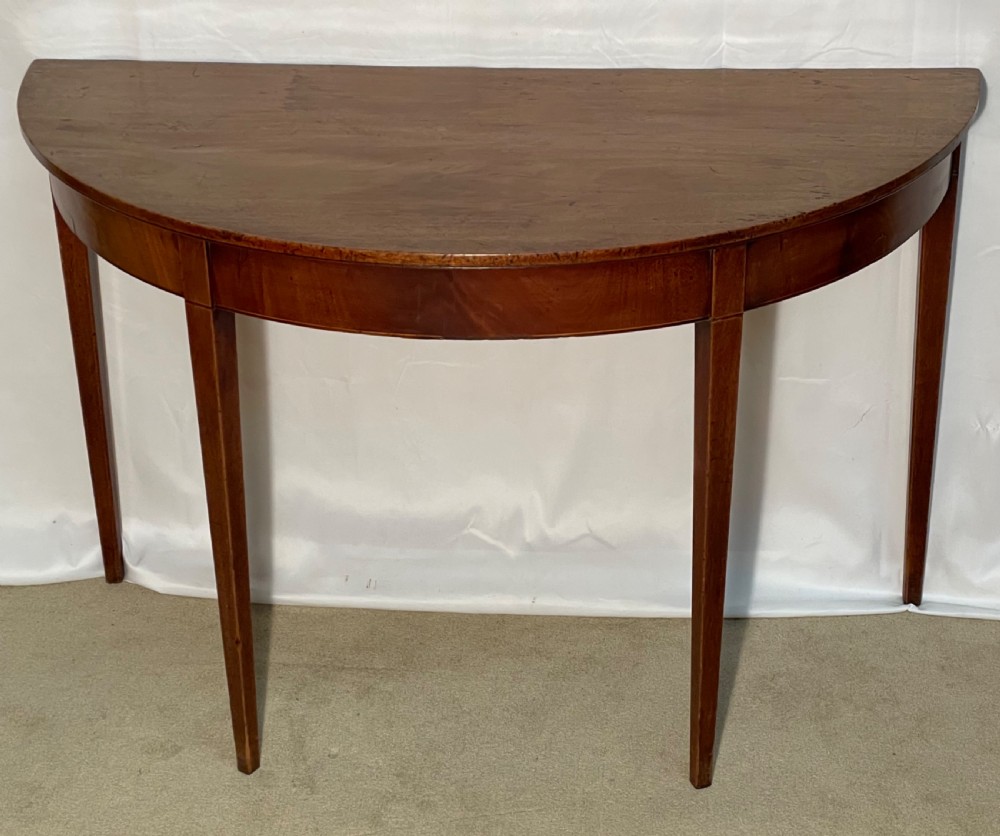 A Georgian mahogany extension dining table featuring a round top assembled from two demi-lune end sections and a central leaf, supported by slender square tapered legs. View VI