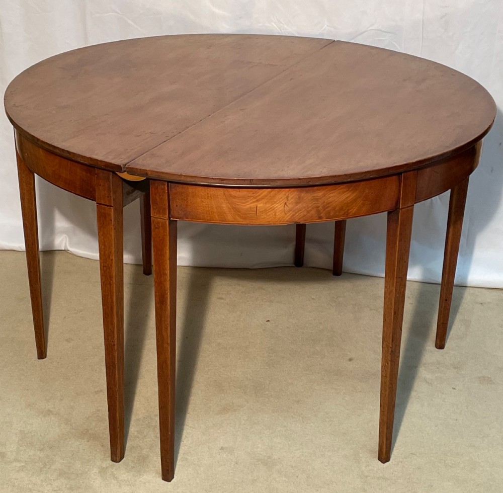 A Georgian mahogany extension dining table featuring a round top assembled from two demi-lune end sections and a central leaf, supported by slender square tapered legs. View IX