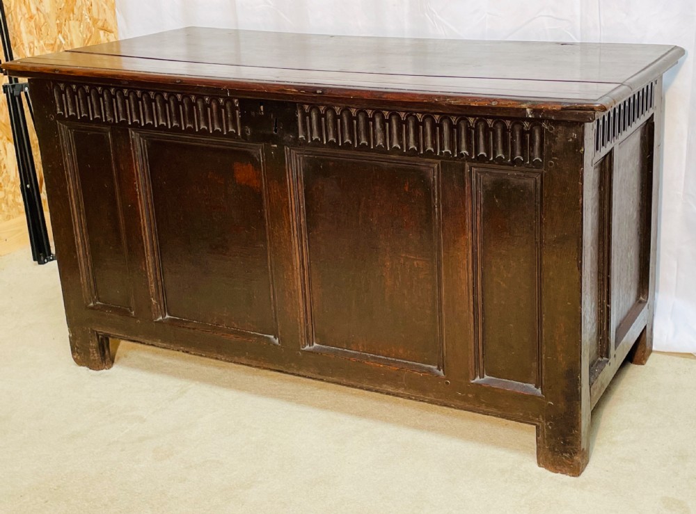 An 18th-century dark oak coffer with a carved upper border and recessed front panels.