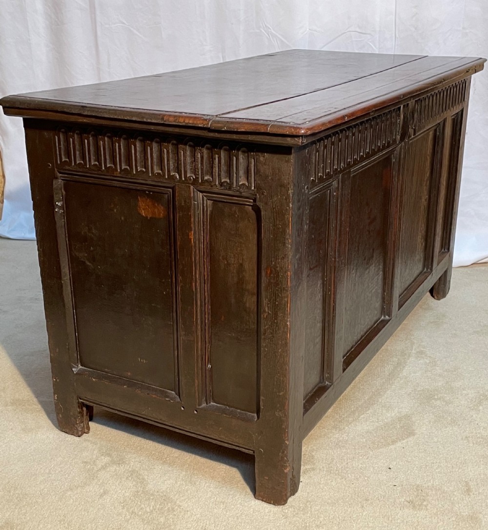 An 18th-century dark oak coffer with a carved upper border and recessed front panels. View X