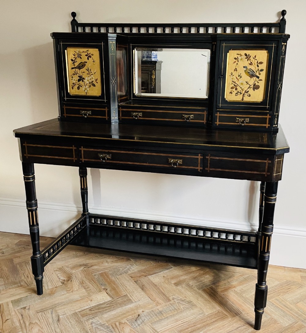 An ebonised Aesthetic Movement bonheur du jour featuring gold line detailing, central mirror, two hand-painted bird panels on small upper cabinets, and turned legs with a spindle lower gallery.