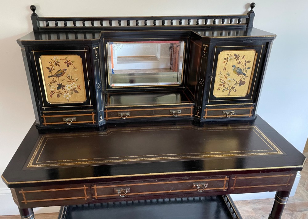 An ebonised Aesthetic Movement bonheur du jour featuring gold line detailing, central mirror, two hand-painted bird panels on small upper cabinets, and turned legs with a spindle lower gallery. View V