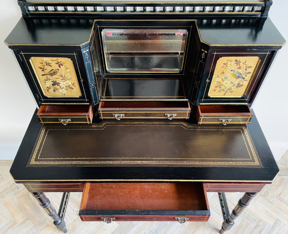 An ebonised Aesthetic Movement bonheur du jour featuring gold line detailing, central mirror, two hand-painted bird panels on small upper cabinets, and turned legs with a spindle lower gallery. View XIII