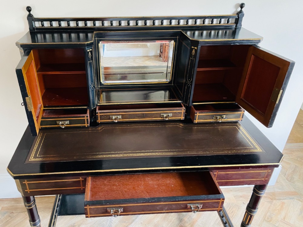 An ebonised Aesthetic Movement bonheur du jour featuring gold line detailing, central mirror, two hand-painted bird panels on small upper cabinets, and turned legs with a spindle lower gallery. View XIV