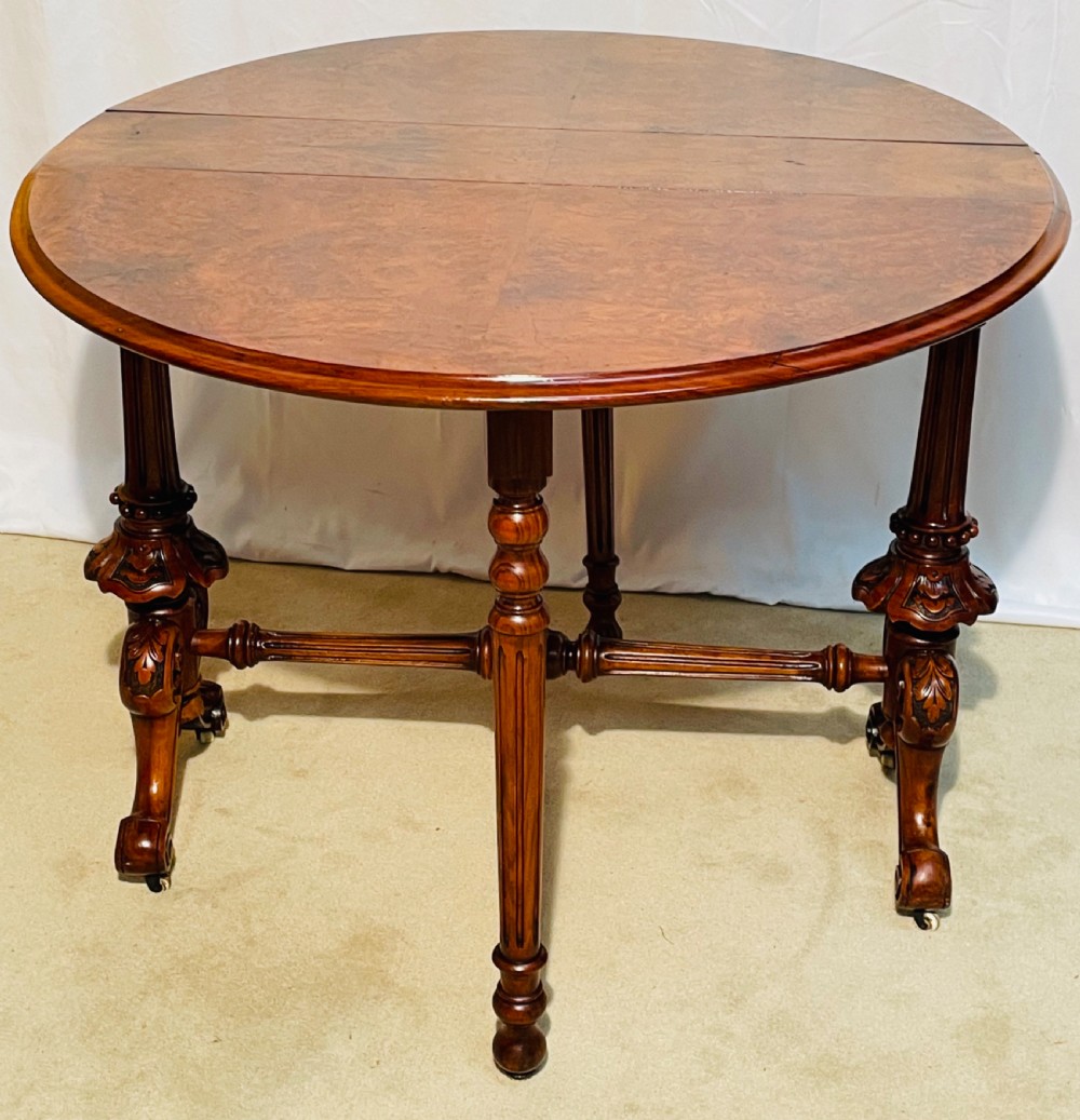 A Victorian burr walnut Sutherland table shown with folded drop leaves, turned end supports, carved cabriole feet, and white ceramic castors. View VIII