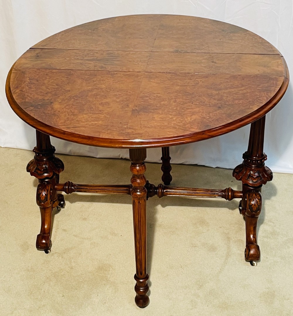 A Victorian burr walnut Sutherland table shown with folded drop leaves, turned end supports, carved cabriole feet, and white ceramic castors. View IX