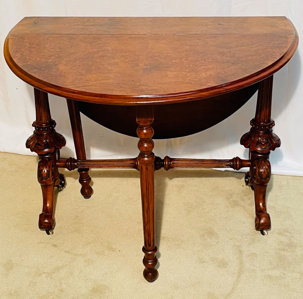 A Victorian burr walnut Sutherland table shown with folded drop leaves, turned end supports, carved cabriole feet, and white ceramic castors. View XI