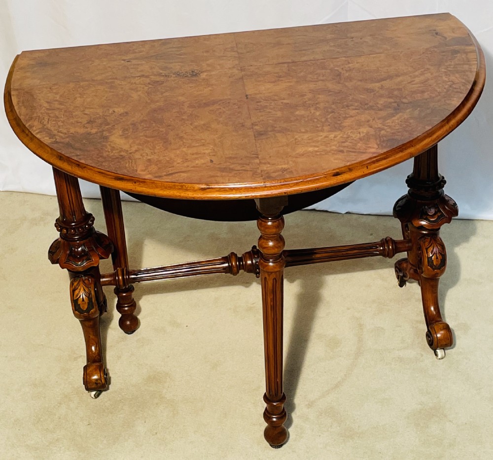 A Victorian burr walnut Sutherland table shown with folded drop leaves, turned end supports, carved cabriole feet, and white ceramic castors. View XIII