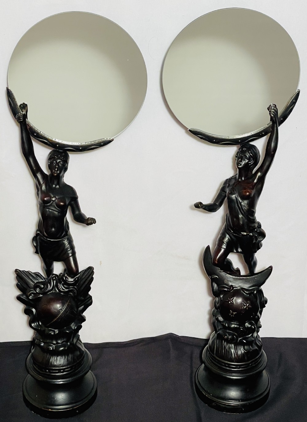 A pair of dark patinated spelter table mirrors featuring classical female figures standing on celestial-themed bases holding circular glass mirrors above their heads. View X