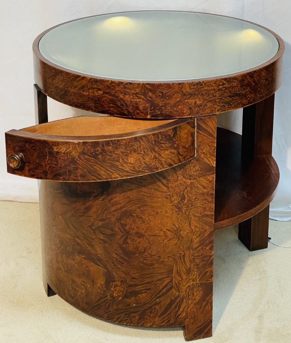A circular Art Deco occasional table made from rich burr walnut veneer featuring an inset illuminated frosted glass top, curved side door, and lower shelf. View VII