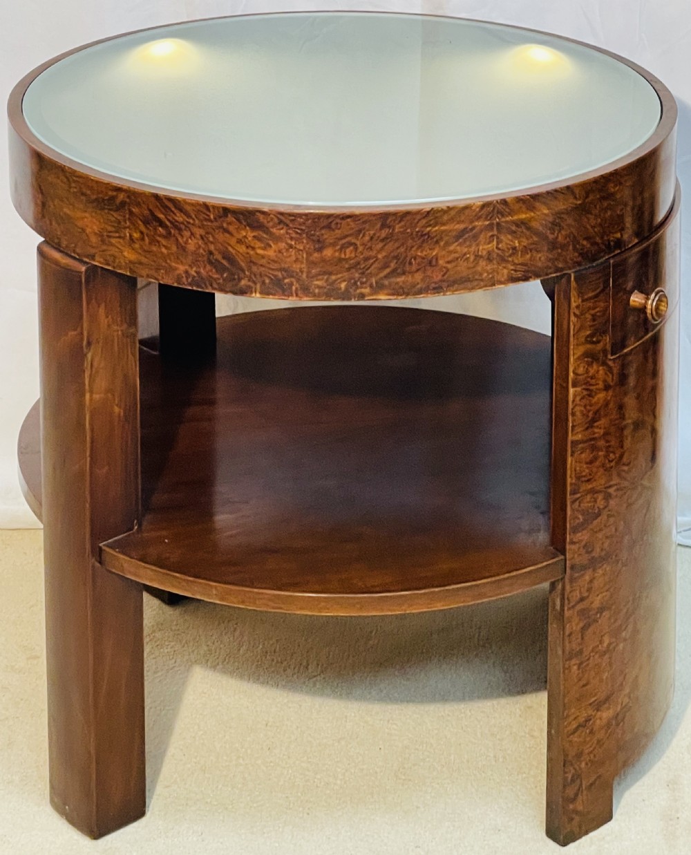 A circular Art Deco occasional table made from rich burr walnut veneer featuring an inset illuminated frosted glass top, curved side door, and lower shelf. View XI