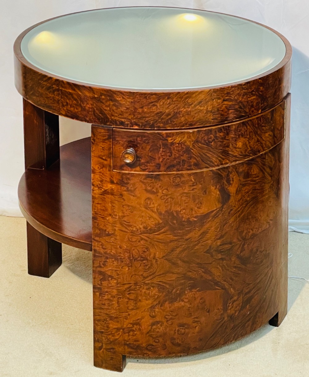 A circular Art Deco occasional table made from rich burr walnut veneer featuring an inset illuminated frosted glass top, curved side door, and lower shelf. View XII
