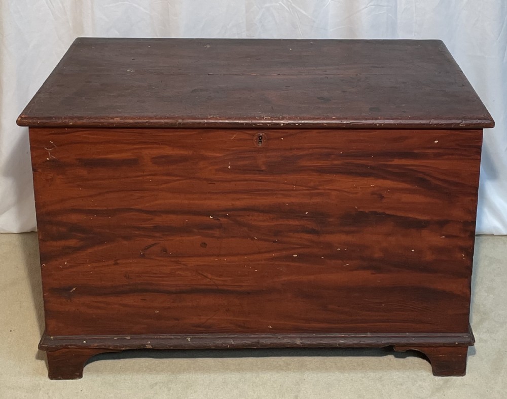 A nineteenth-century rectangular pine blanket box with a reddish-brown painted finish, hinged lid, keyhole, and bracket feet.