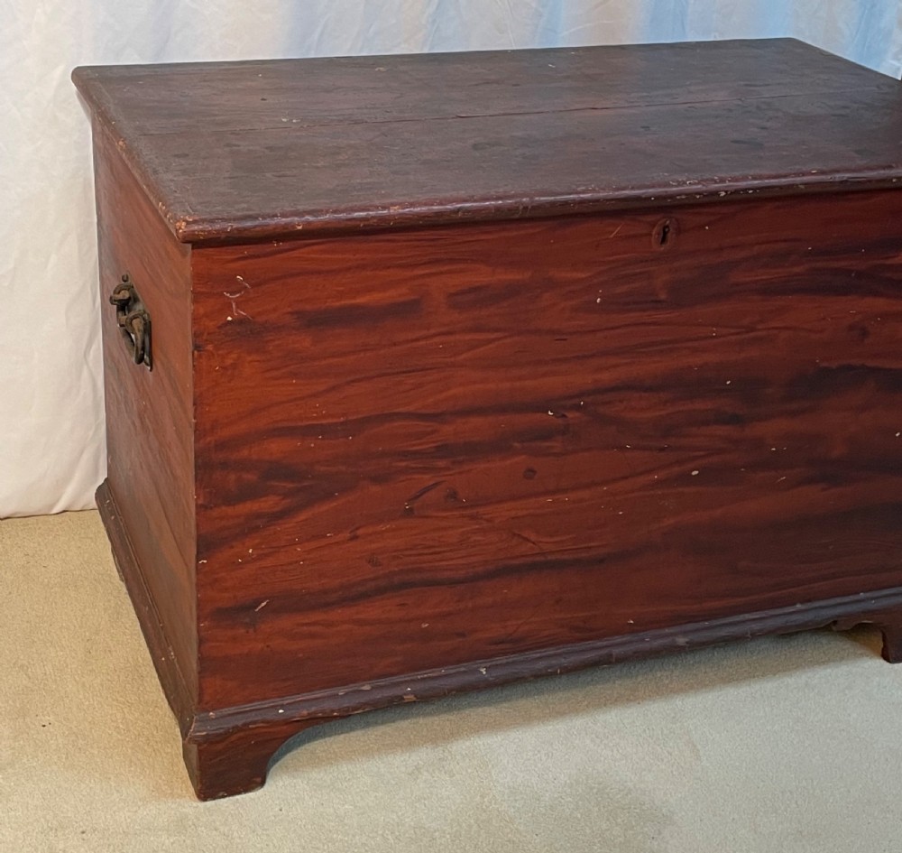A nineteenth-century rectangular pine blanket box with a reddish-brown painted finish, hinged lid, keyhole, and bracket feet. View VII