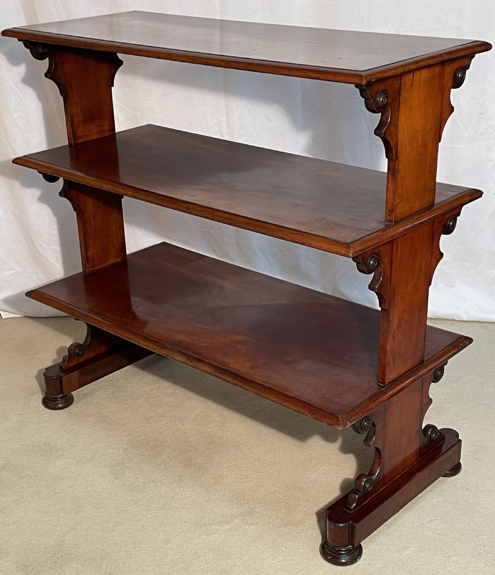 A three-tiered William IV mahogany dumb waiter featuring carved scroll supports with carved roundel details and a polished finish. View III