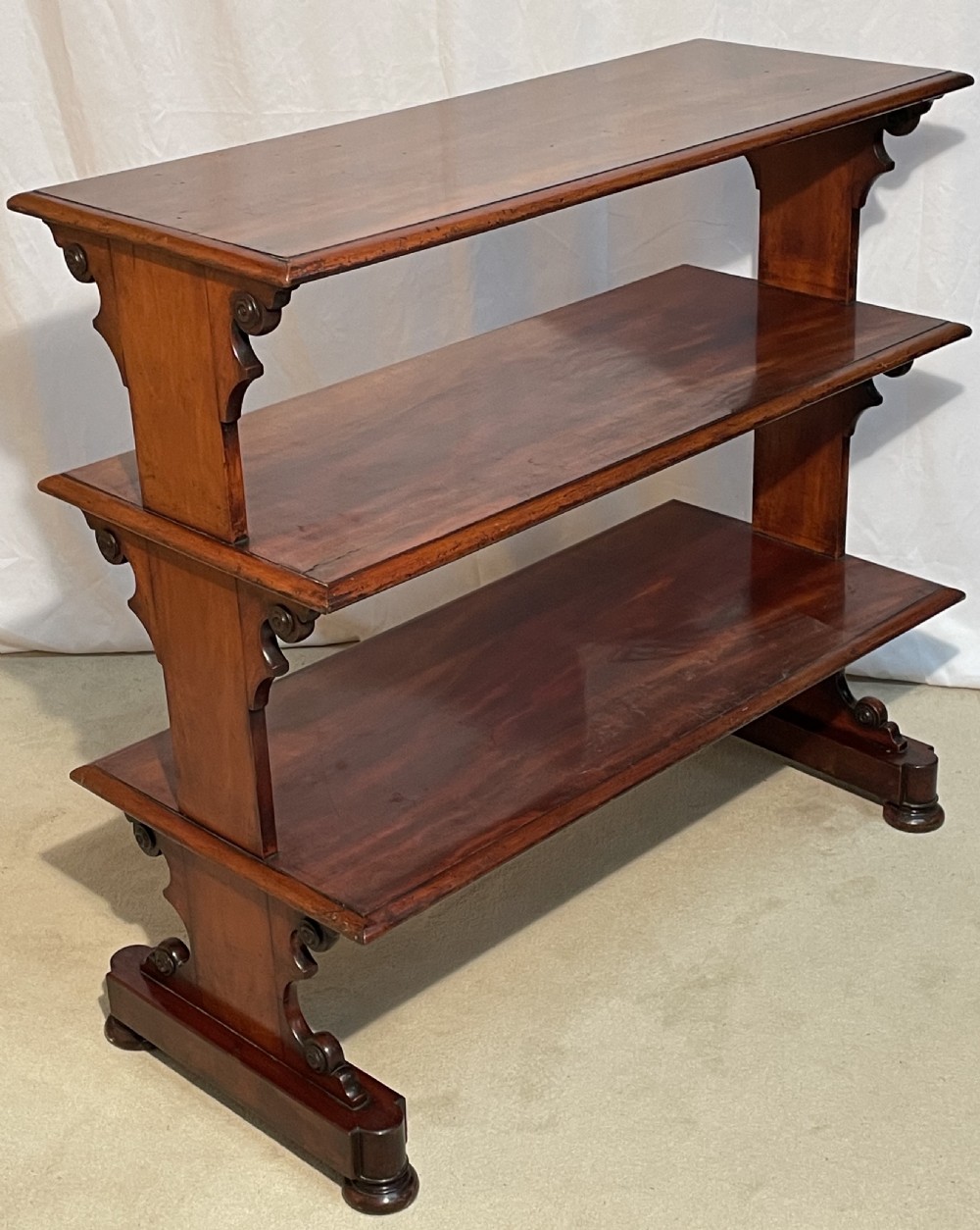 A three-tiered William IV mahogany dumb waiter featuring carved scroll supports with carved roundel details and a polished finish. View V