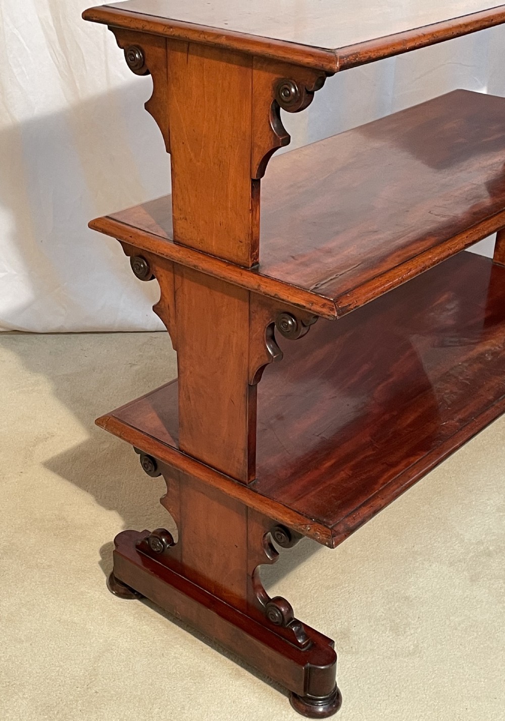 A three-tiered William IV mahogany dumb waiter featuring carved scroll supports with carved roundel details and a polished finish. View VIII