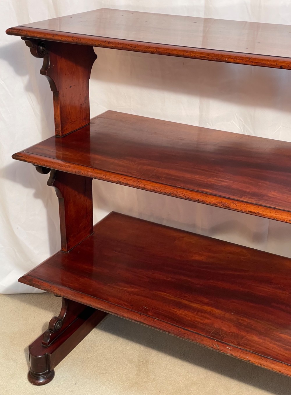 A three-tiered William IV mahogany dumb waiter featuring carved scroll supports with carved roundel details and a polished finish. View XIII