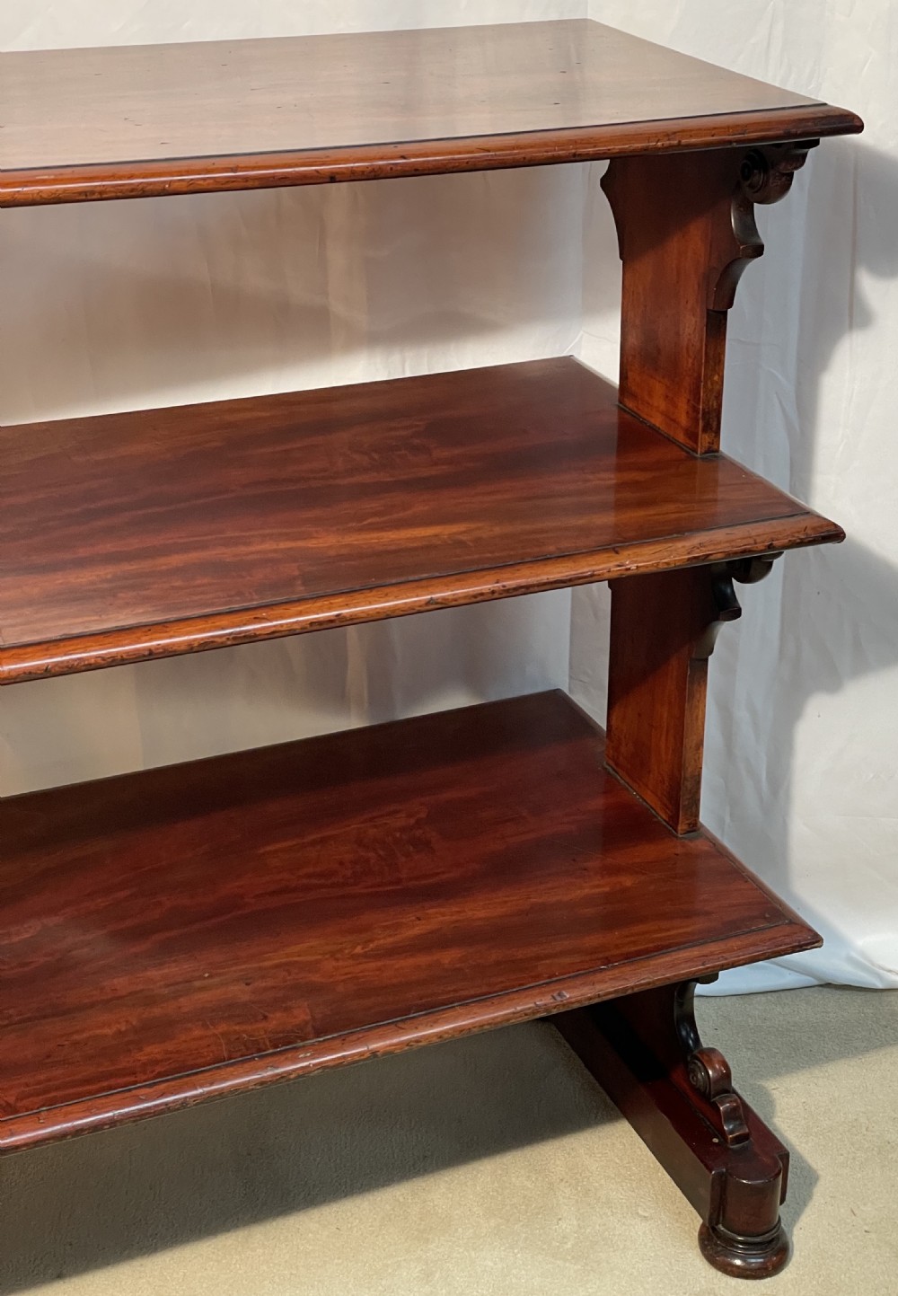 A three-tiered William IV mahogany dumb waiter featuring carved scroll supports with carved roundel details and a polished finish. View XIV