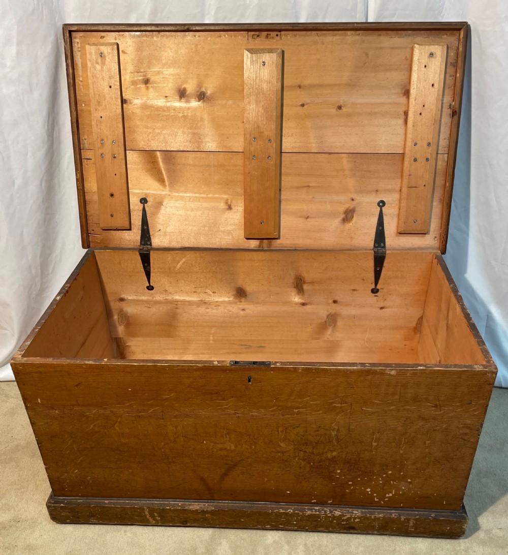 An open antique pine blanket box with a faux-grain painted exterior, exposed internal timber, and iron strap hinges.