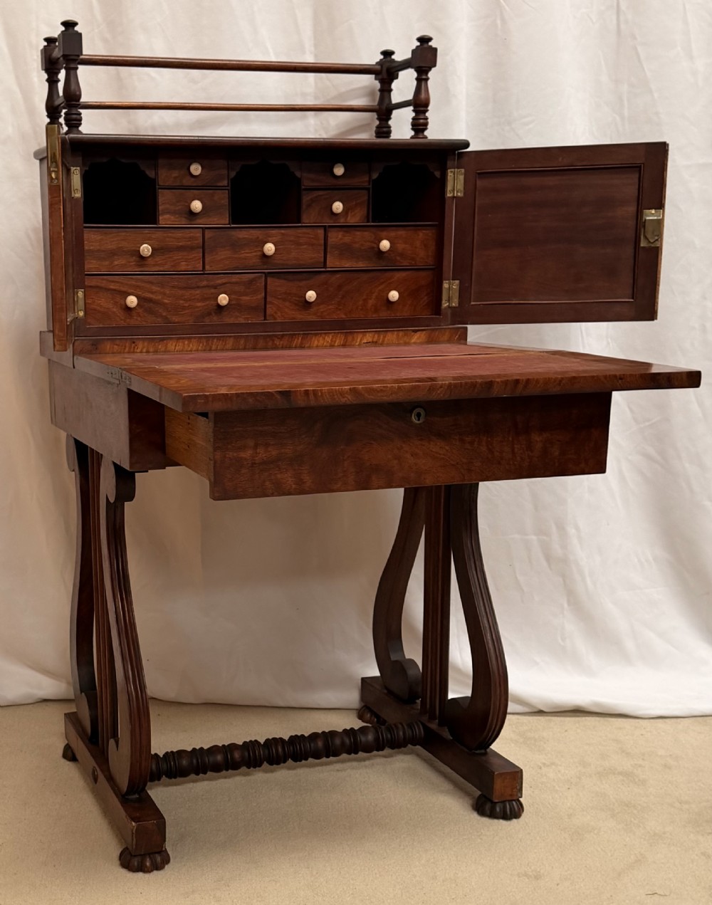 A dark mahogany Regency writing desk featuring twin lyre-shaped end supports, a fold-out leather-lined writing surface, and an upper cabinet with small fitted drawers.