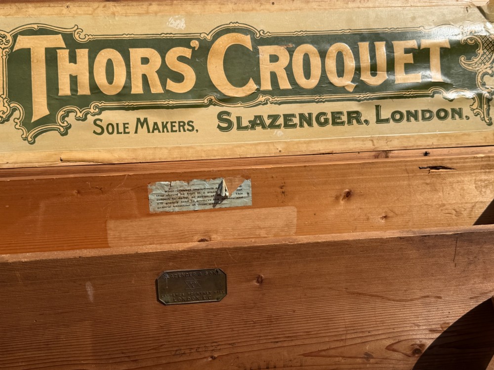 An open pine storage box with a Slazenger printed label displaying four wooden croquet mallets, coloured balls, metal hoops, and wooden pegs. View III
