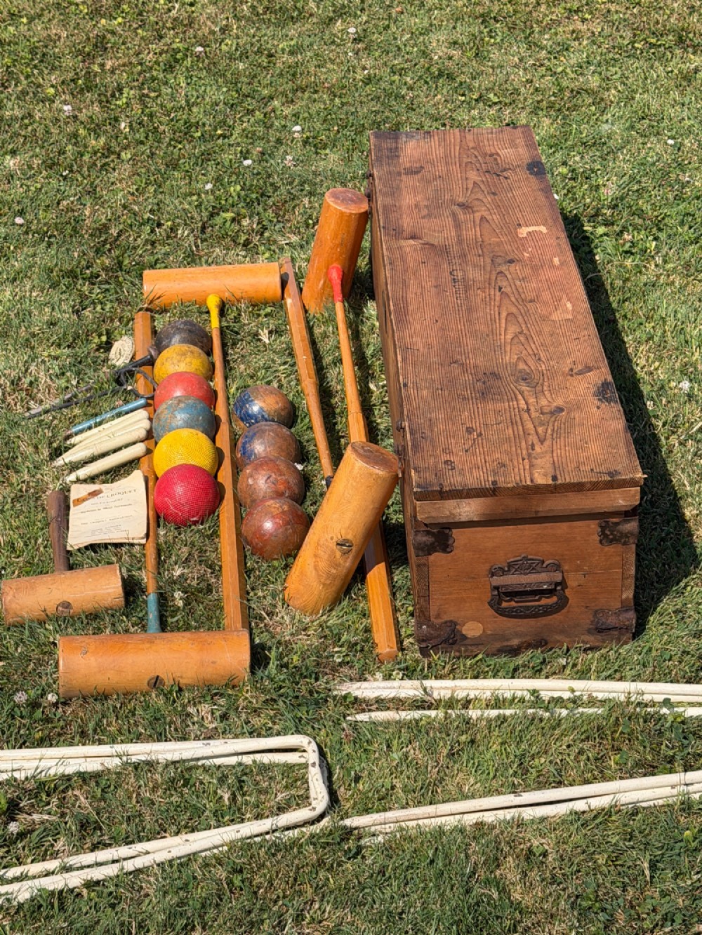 An open pine storage box with a Slazenger printed label displaying four wooden croquet mallets, coloured balls, metal hoops, and wooden pegs. View IV