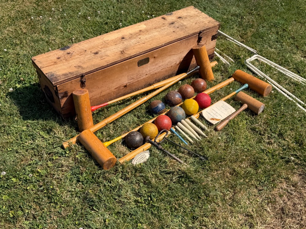 An open pine storage box with a Slazenger printed label displaying four wooden croquet mallets, coloured balls, metal hoops, and wooden pegs. View VI