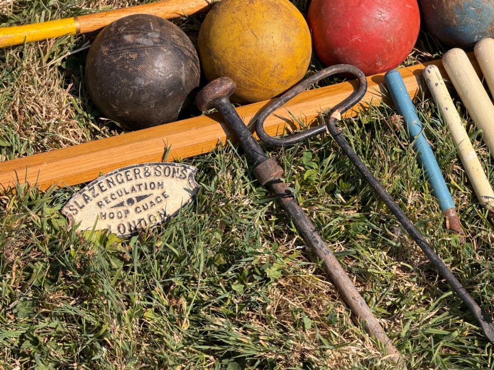 An open pine storage box with a Slazenger printed label displaying four wooden croquet mallets, coloured balls, metal hoops, and wooden pegs. View VII