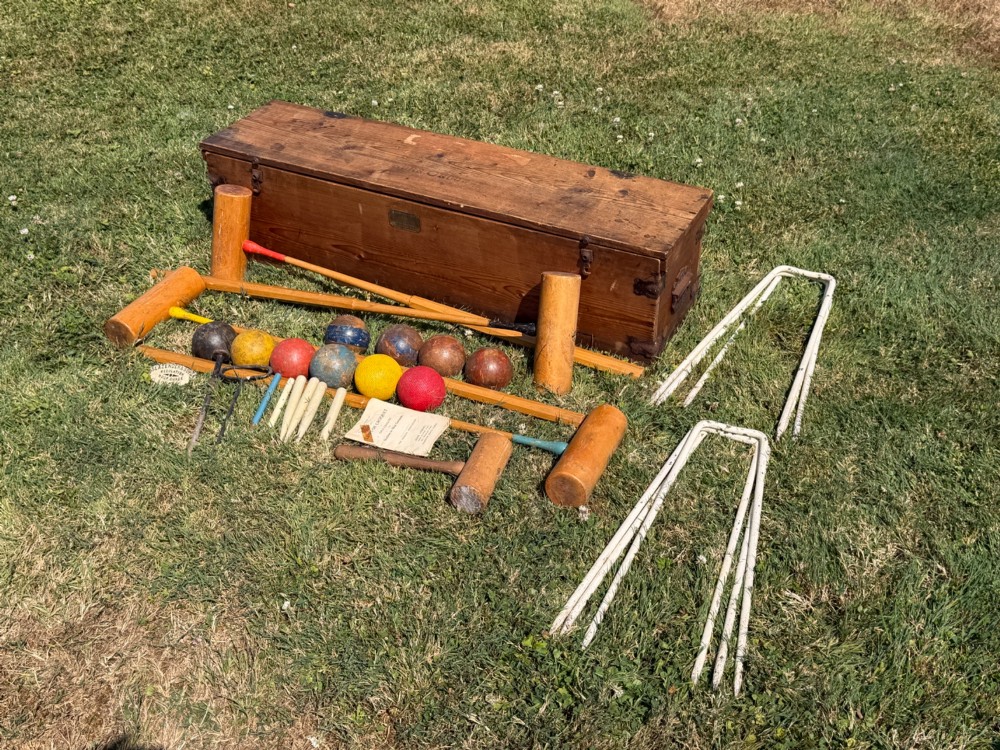 An open pine storage box with a Slazenger printed label displaying four wooden croquet mallets, coloured balls, metal hoops, and wooden pegs. View IX